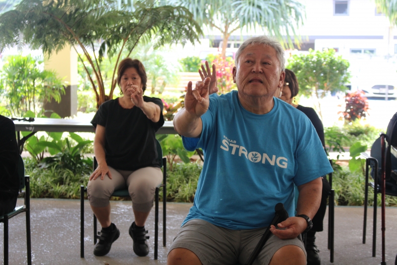 elderly people sitting in chairs with their arms extended