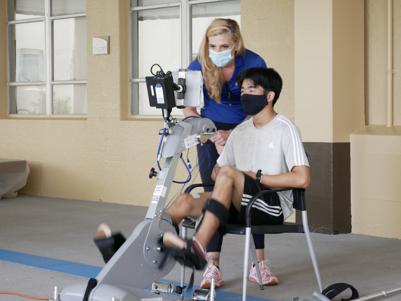 staff helping young man use an electric stimulation bike