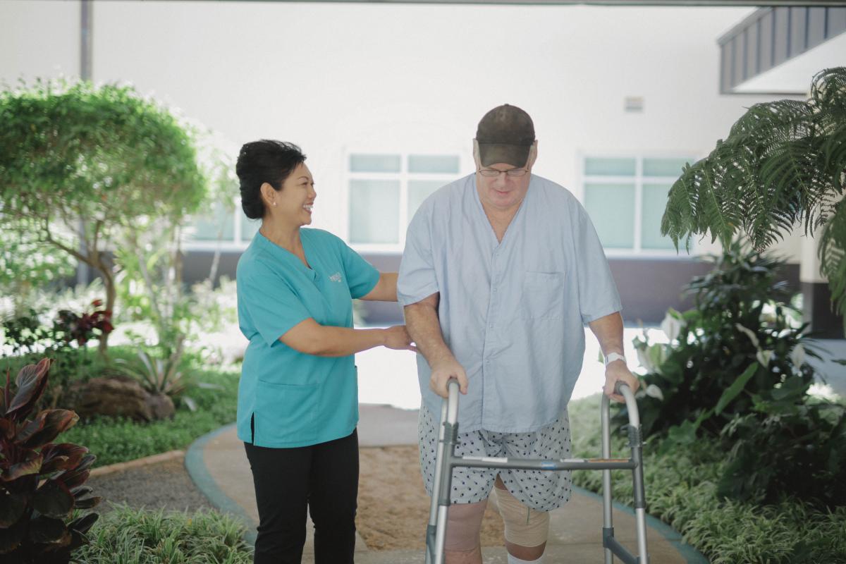nurse helping man walk with walker